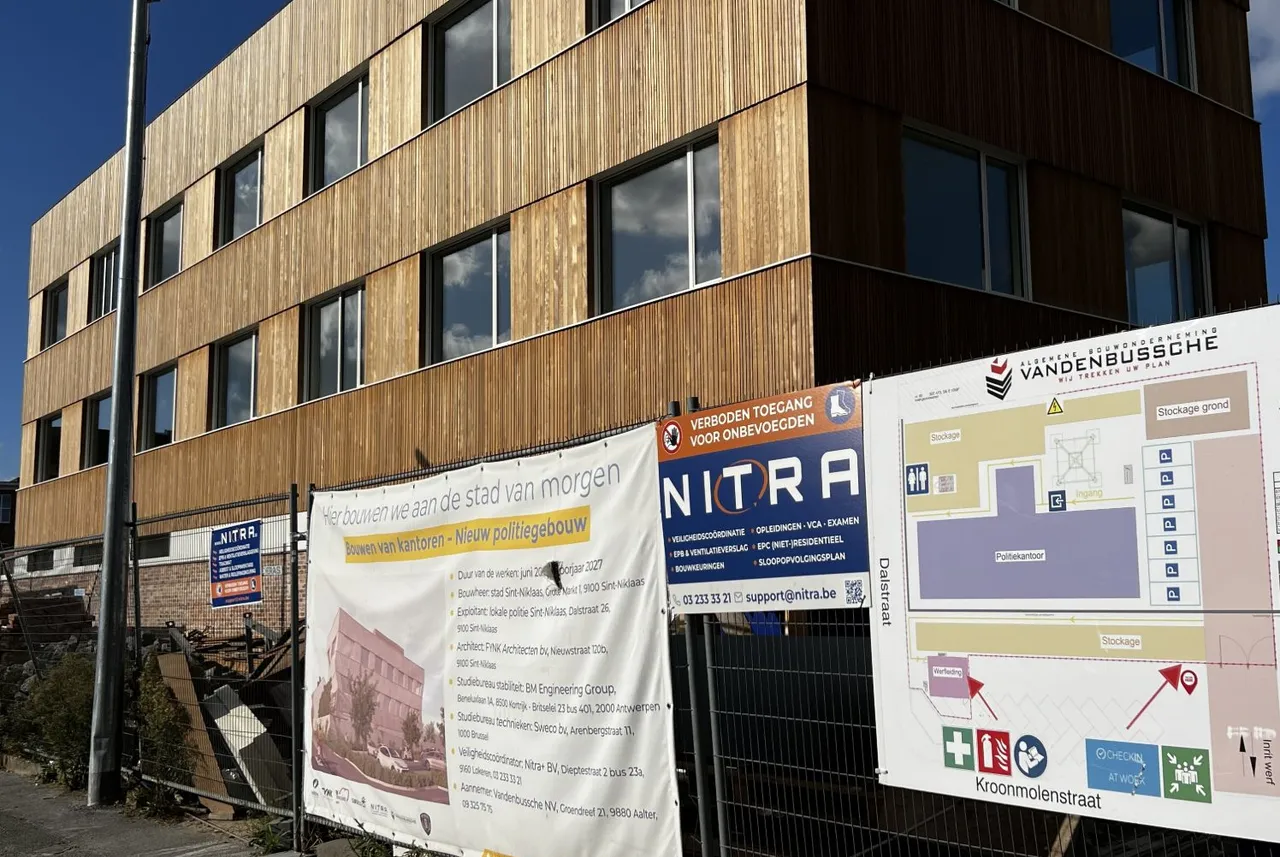 Het nieuwe politiegebouw in Sint-Niklaas met houten gevel, met aan de werfomheining het Nitra-bord en het werfplan